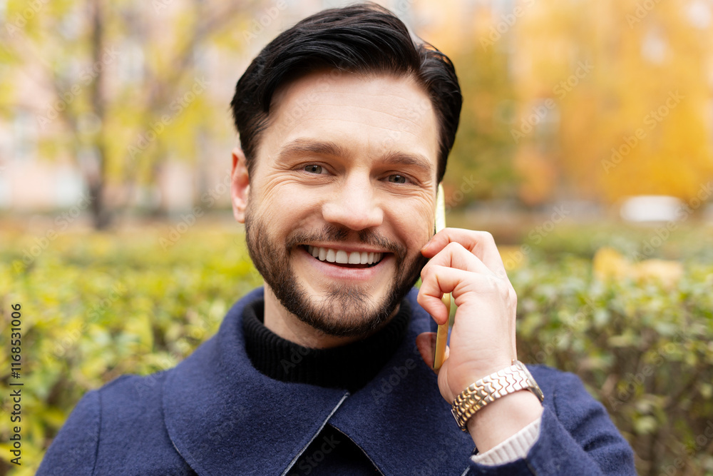 Smiling young bearded man talking on smartphone looking at camera on the street Smiling young bearded man talking on smartphone looking at camera on the street