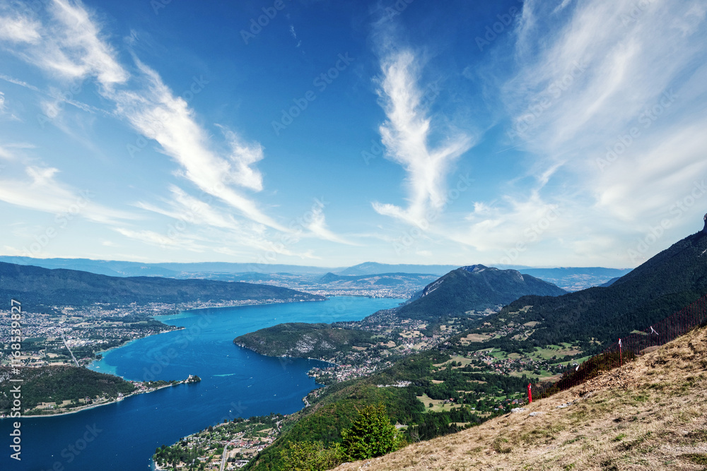 Beautiful view of a lake of Annecy with mountains in the background. The sky is mostly clear with a few clouds scattered around Beautiful view of a lake of Annecy with mountains in the background. The sky is mostly clear with a few clouds scattered around
