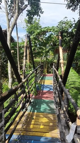 A person walking through the colorful wooden bridge over a forest. The bridge is made of wood and has a rainbow of colors