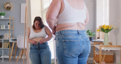 Pleasant obese woman posing in front of mirror at home, chubby overweight plus size big fat fit lady doing waist measurement with progress in weight loss after sport, dieting, looking in despair 