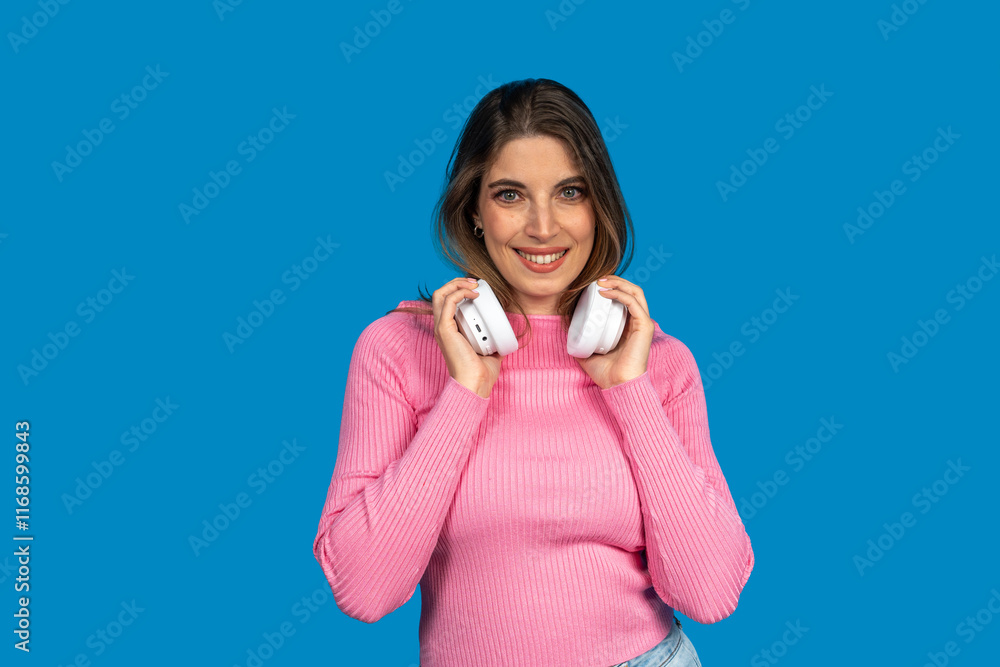 Young woman holding white wireless headphones on blue background Young woman holding white wireless headphones on blue background