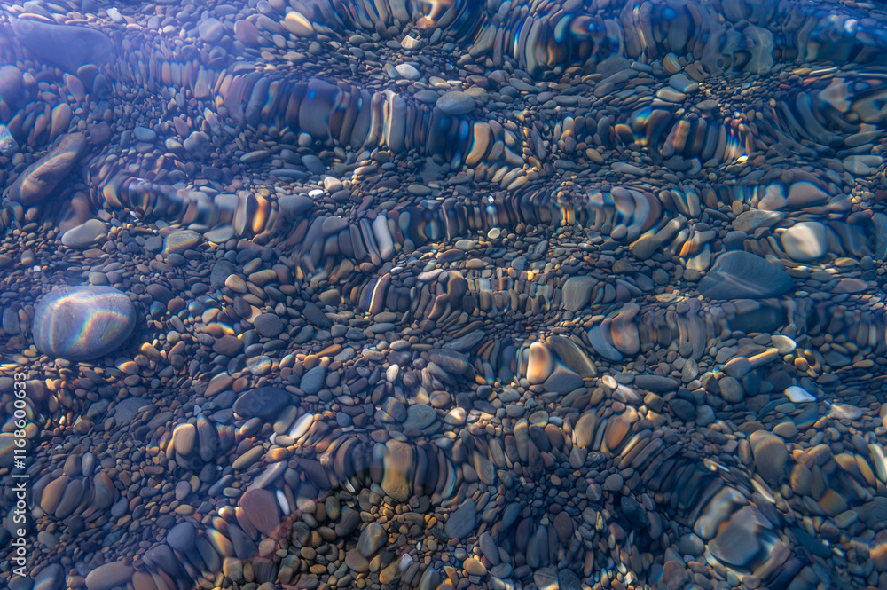 Underwater pebble backgrounds. Colorful stones sea bottom in the sun rays. View from above through clear water. Seascape wallpaper texture. Defocus.