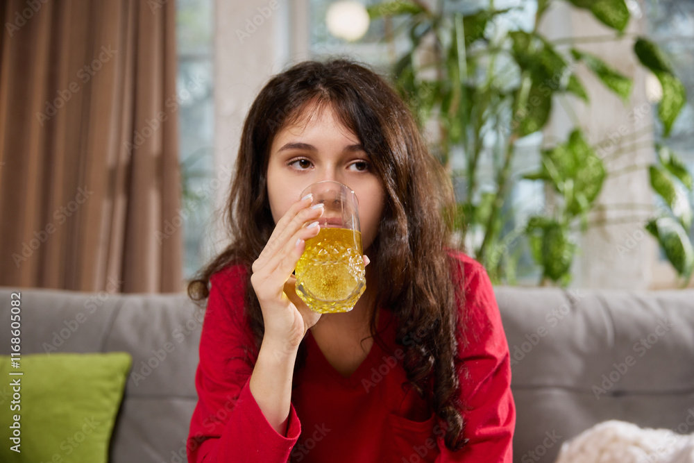 Woman in red pajama holds small white packet close to camera while sitting on couch with green pillow and kettle nearby. Concept of illness, health insurance, pharmaceutical, medicine. Ad. Woman in red pajama holds small white packet close to camera while sitting on couch with green pillow and kettle nearby. Concept of illness, health insurance, pharmaceutical, medicine. Ad.