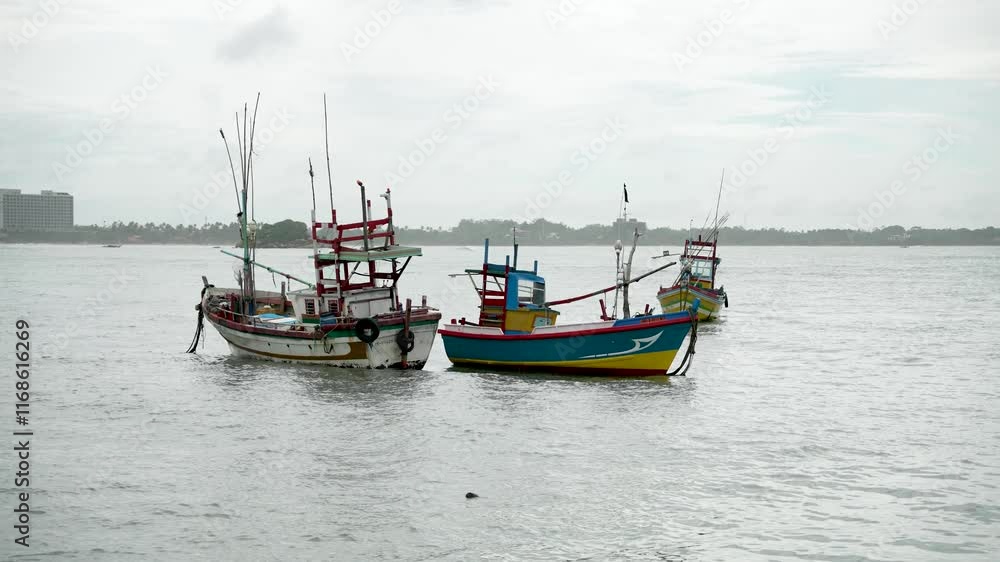Vibrant and traditional small fishing boats gently floating near the coast on a cloudy day by calm waters, reflecting the serene yet industrious culture of coastal livelihoods. Vibrant and traditional small fishing boats gently floating near the coast on a cloudy day by calm waters, reflecting the serene yet industrious culture of coastal livelihoods.