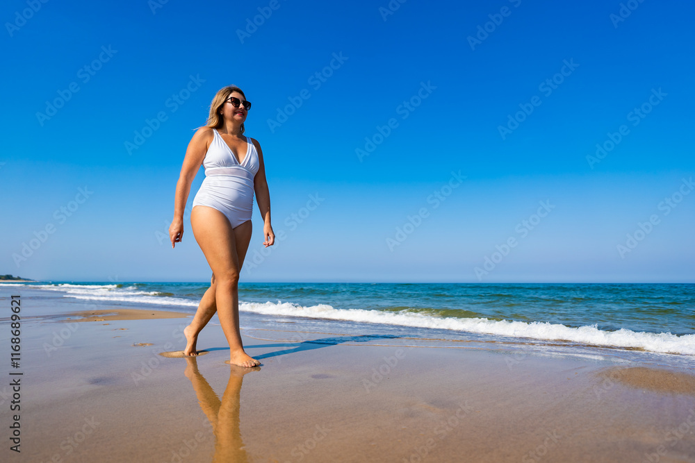 Summertime by sea. Beautiful middle-aged woman walking on sandy beach on sunny summer day. Front view Summertime by sea. Beautiful middle-aged woman walking on sandy beach on sunny summer day. Front view