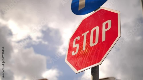 Stop sign with blue directional arrow against cloudy sky, perfect for road safety campaigns, driver education materials, traffic regulation content and urban infrastructure presentations