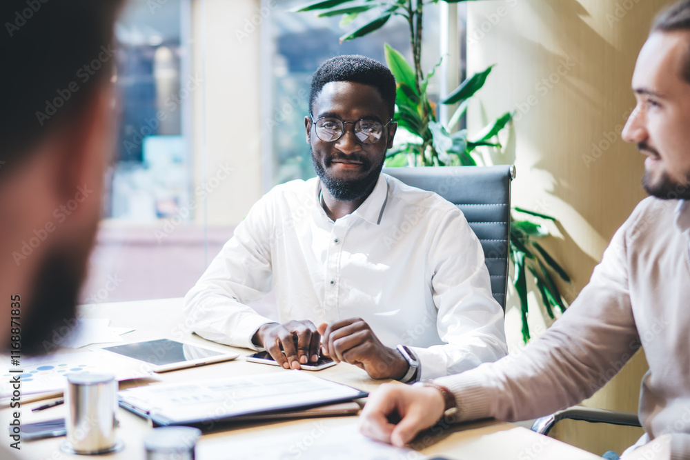 Selective focus on successful African American man in optical spectacles for eyes protection, diverse male partners brainstorming on startup project during working process in office interior Selective focus on successful African American man in optical spectacles for eyes protection, diverse male partners brainstorming on startup project during working process in office interior