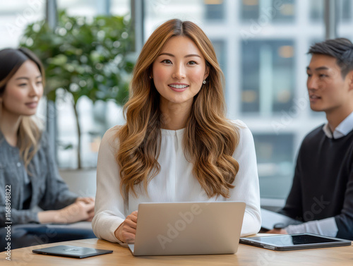Wallpaper Mural A bright, modern office with three professionals sitting at a round table, discussing a project. A woman in a white blouse points at a laptop screen while explaining something to two colleague Torontodigital.ca