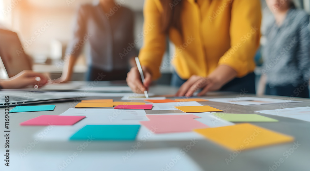 Fototapeta premium A collaborative workspace with people brainstorming and organizing ideas using colorful sticky notes on a table.