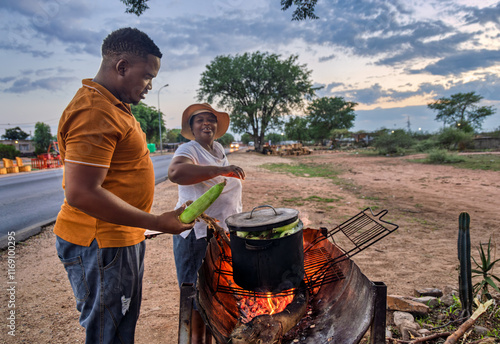 Fotografie African street vendor, woman selling boiled corn to a young customer client , ma