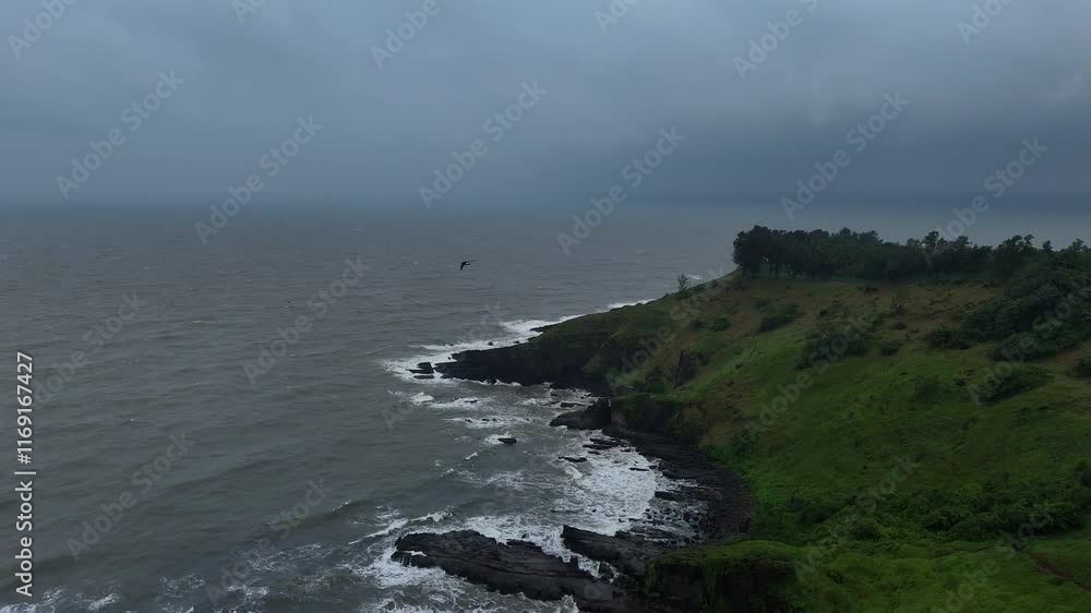 Drone pullback of a green cliffy beach with calm ocean and cloudy sky in Goa, Candolim, India Drone pullback of a green cliffy beach with calm ocean and cloudy sky in Goa, Candolim, India