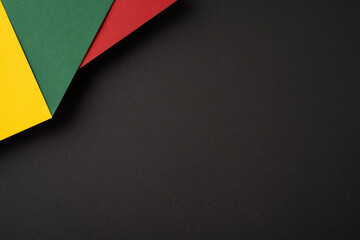Abstract composition featuring red, green, and yellow paper sheets overlapping on a dark backdrop, creating contrast