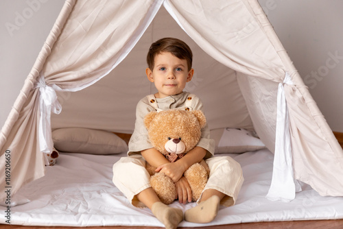 Happy 5 years old little boy sitting in a wigwam tent, hugging soft toy teddy bear. Children's room, childhood, games, imagination. High quality photo photo