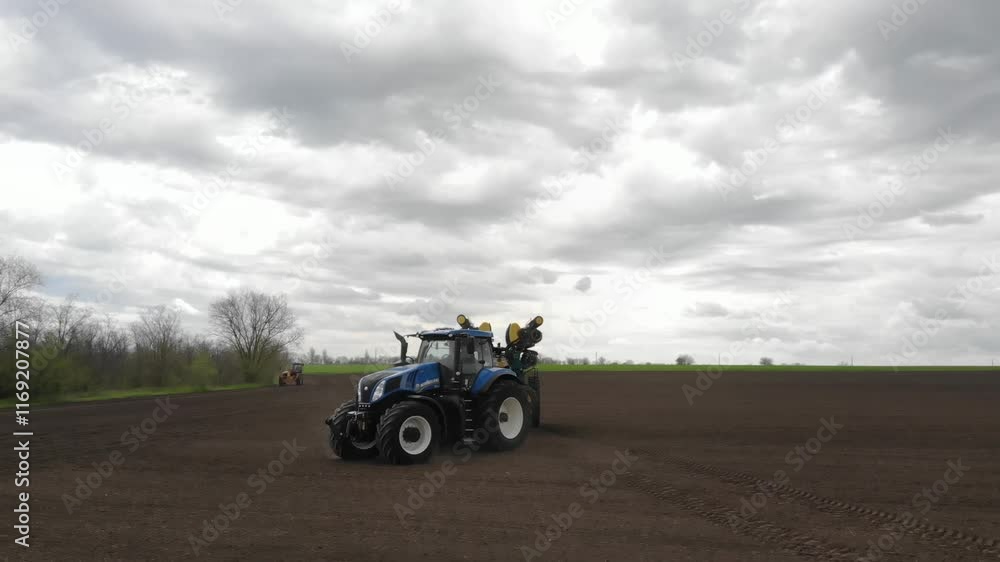 Blue tractor with yellow seeder working on the field Blue tractor with yellow seeder working on the field