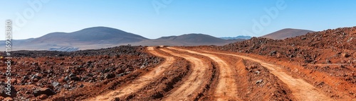 A winding dirt road stretches through a rugged landscape, surrounded by mountains under a clear blue sky.