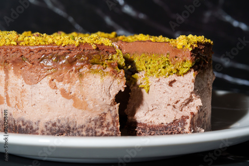 Slice of chocolate Dubai cheesecake with pistachio paste and kataifi dough filling covered in chocolate ganache on white plate. Close up. Indulgence, gourmet desserts, art of culinary presentation photo