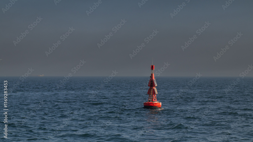 Red buoy floating in the ocean close to coast. Navigating beacon in the sea for ships and other vessels