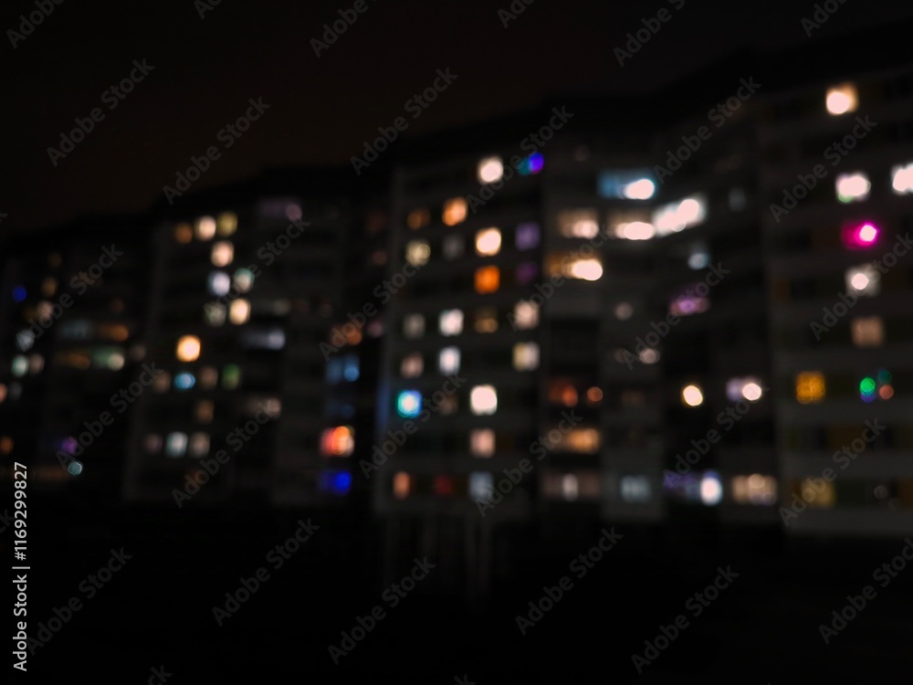 Fototapeta premium Night urban landscape. Bright light of different colors from the windows of a multi-storey building, blurred. The lights are on in the windows of the houses at night