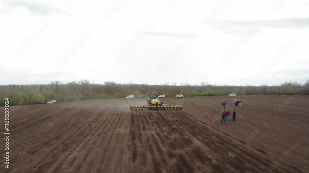 Blue tractor with yellow seeder working on the field Blue tractor with yellow seeder working on the field