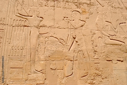 Carved hieroglyphics and ancient reliefs etched into a sandstone temple wall, depicting historical Egyptian figures and symbols. photo