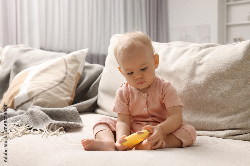Cute little baby with rattle on sofa indoors Cute little baby with rattle on sofa indoors