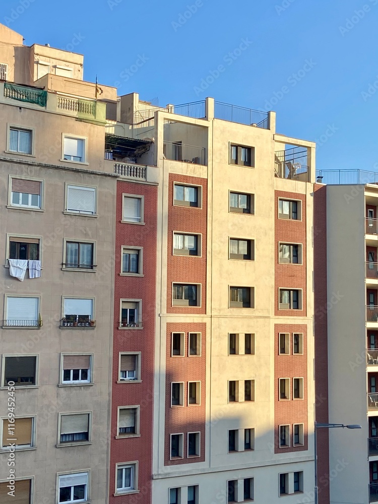 Facade of a multi-story residential building with beige, orange, and red tones under a clear blue sky. Barcelona, Spain Facade of a multi-story residential building with beige, orange, and red tones under a clear blue sky. Barcelona, Spain