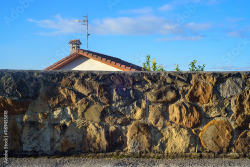 Tejado de chalet asomando por encima de muro de piedra photo