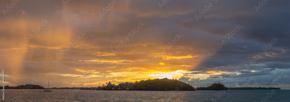 A serene and picturesque scene of Bora Bora at sunset, a sailboat is anchored in the calm ocean waters, with the lush, green island and its mountainous terrain in the background.