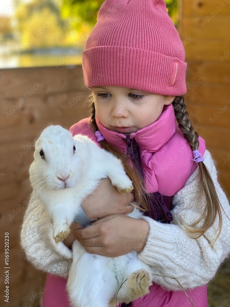 A little girl with blue eyes, wearing a pink vest and a pink hat, standing outdoors on a sunny day. She is holding a large, fluffy white rabbit with blue eyes. The sunlight creates a warm atmosphere, A little girl with blue eyes, wearing a pink vest and a pink hat, standing outdoors on a sunny day. She is holding a large, fluffy white rabbit with blue eyes. The sunlight creates a warm atmosphere,