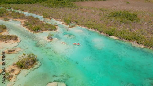 Toma aérea de dron de una pareja de jóvenes navegando tranquilamente en kayak en un río color turquesa de los Rápidos de Bacalar en México