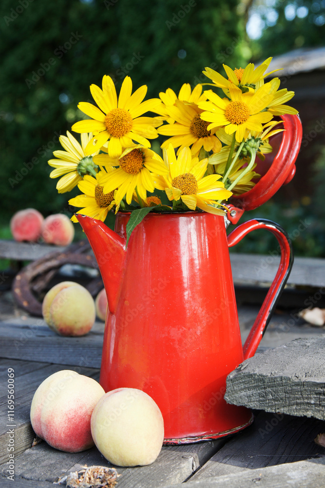 Bouquet of yellow wildflowers in a red watering can on a wooden table.