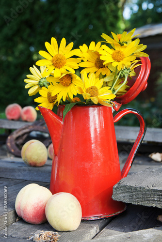 Bouquet of yellow wildflowers in a red watering can on a wooden table.