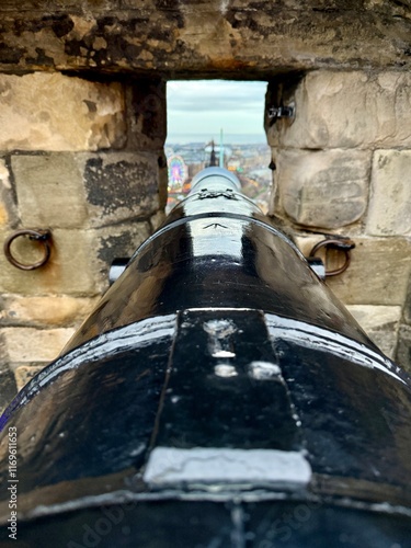 фотографія Black cannon aimed through a castle embrasure, overlooking a fairground in the distance