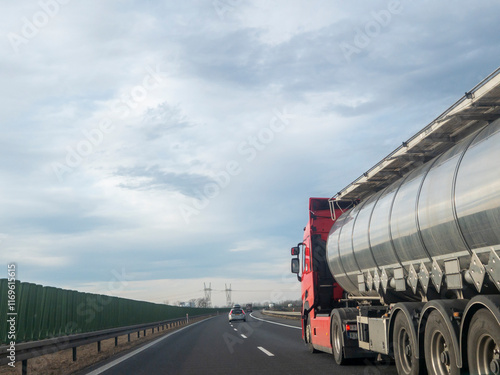 A red tanker truck traveling on a highway, showcasing the transportation of goods. The road stretches towards the horizon under a cloudy sky. photo