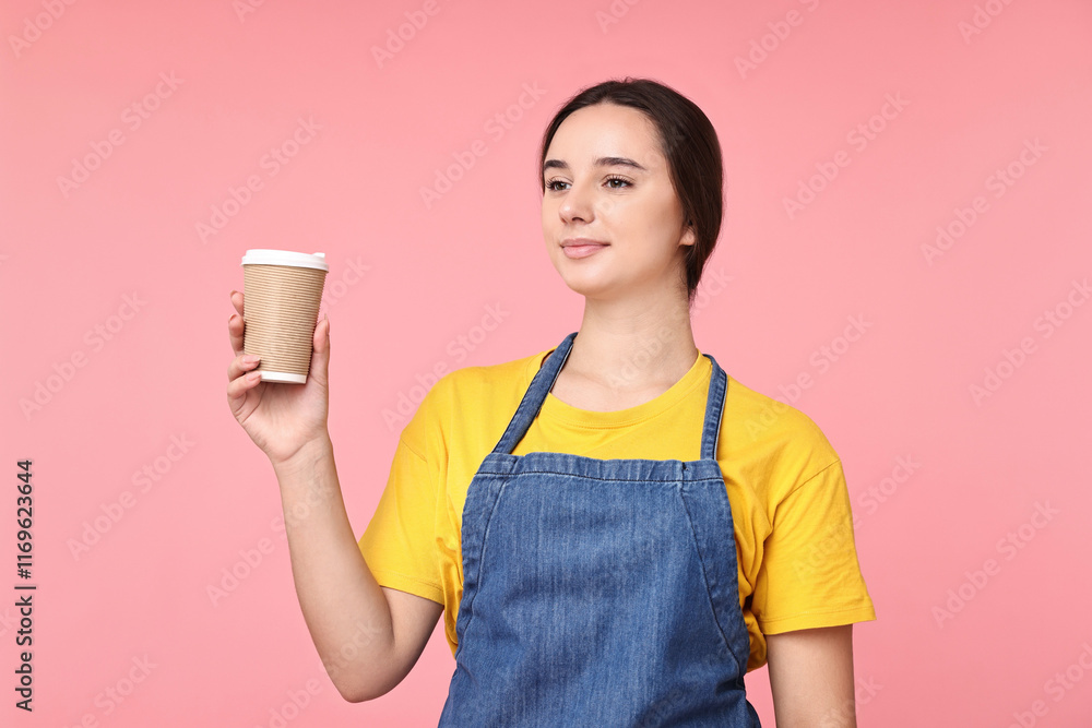 Girl in apron with paper cup of coffee on pink background. Work for teenagers Girl in apron with paper cup of coffee on pink background. Work for teenagers