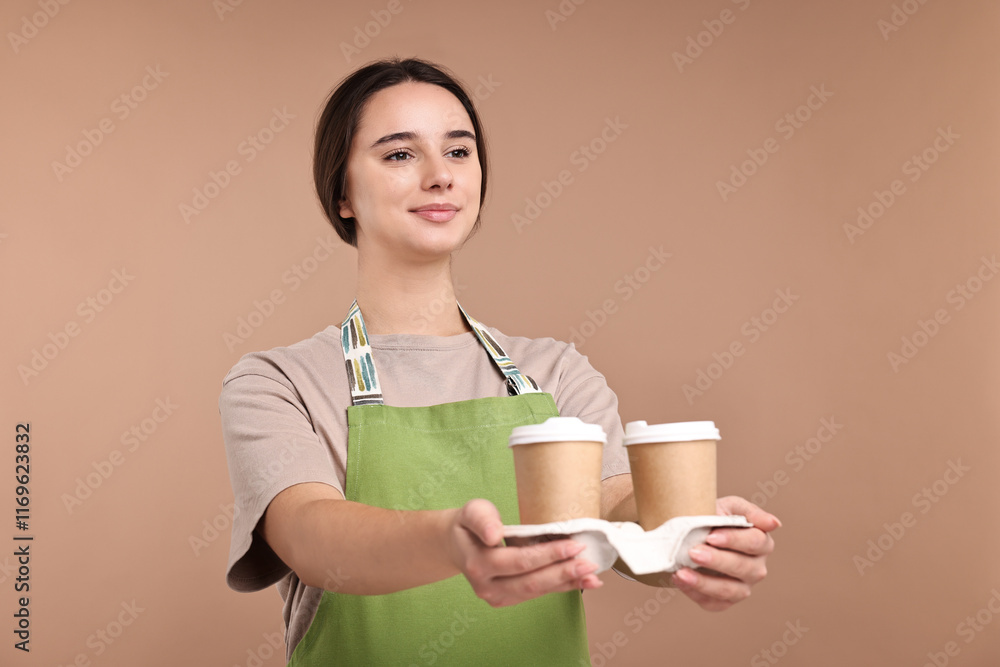 Girl in apron with takeaway paper cups of coffee on pale brown background. Work for teenagers Girl in apron with takeaway paper cups of coffee on pale brown background. Work for teenagers