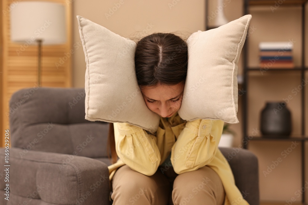 Obraz premium Annoyed woman covering her ears with pillows due to loud sound at home