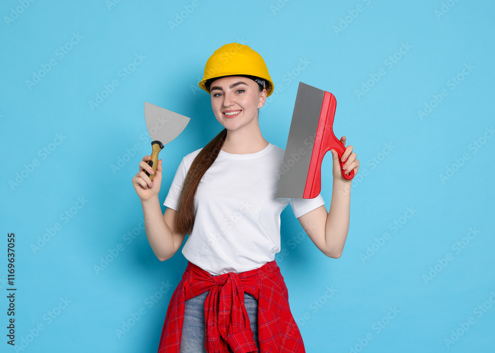 Portrait of young decorator with putty knives on light blue background Portrait of young decorator with putty knives on light blue background