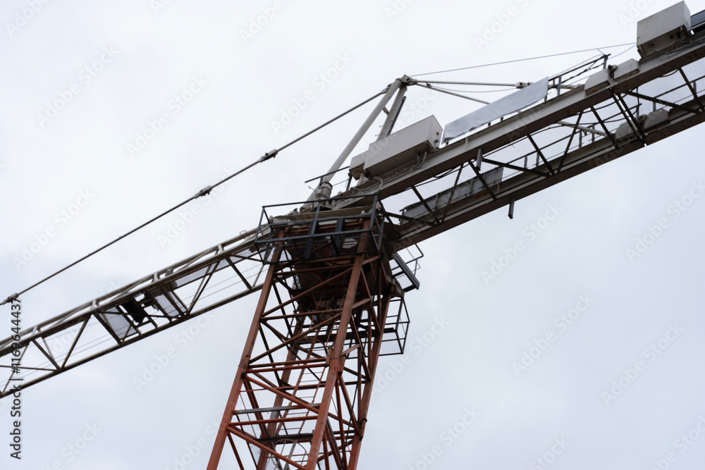 A detailed view of a tall construction crane against a pale sky. The photograph emphasizes the geometric structure of the crane, showcasing its intricate design and industrial purpose. A detailed view of a tall construction crane against a pale sky. The photograph emphasizes the geometric structure of the crane, showcasing its intricate design and industrial purpose.