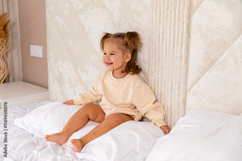 Happy baby in bed. Cute little newborn girl in bodysuit with smiling face on bed in bedroom. Infant baby resting, playing sitting on white bed linen at home. Motherhood and childcare concept Happy baby in bed. Cute little newborn girl in bodysuit with smiling face on bed in bedroom. Infant baby resting, playing sitting on white bed linen at home. Motherhood and childcare concept