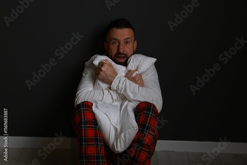 Fear of darkness. Scared man hugging pillow indoors at night photo