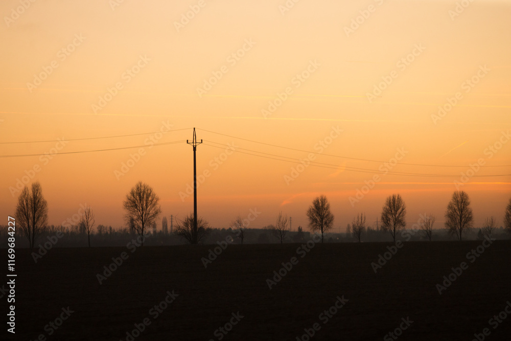 Silhouetted trees and a power pole standing tall against a beautiful sunset sky filled with vibrant hues, creating a peaceful scene Silhouetted trees and a power pole standing tall against a beautiful sunset sky filled with vibrant hues, creating a peaceful scene