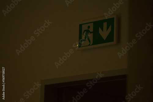 Dark green exit sign is mounted on wall at night, clearly indicating direction for safe exit from premises. Safety and compliance with building regulations, blending functionality with simple design. photo