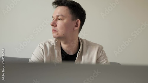 Young man feeling upset while working on laptop in a modern home interior. Depressed businessman looking frustrated.