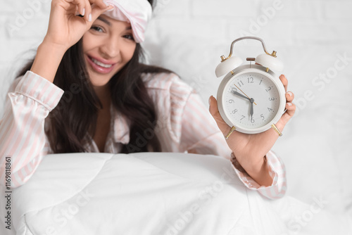 Awake young woman with sleeping mask and alarm clock in bedroom, closeup photo