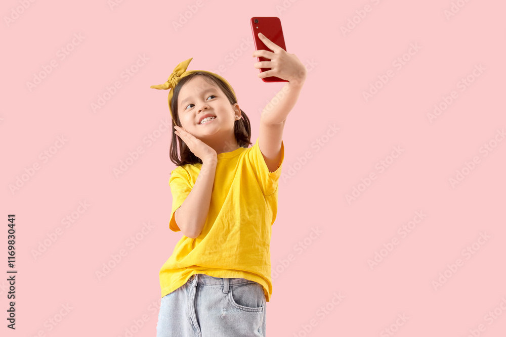 Cute little Asian girl with mobile phone taking selfie on pink background Cute little Asian girl with mobile phone taking selfie on pink background