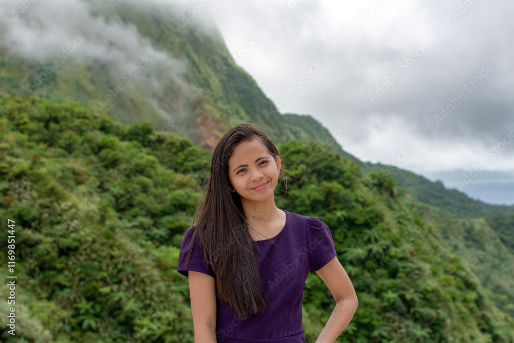 Naklejka premium Portrait of a beautiful young Filipina woman against the backdrop of tropical mountains covered with clouds