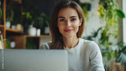 confident woman smiles while working on laptop in bright, green filled office. Her professional demeanor reflects positive and productive atmosphere photo