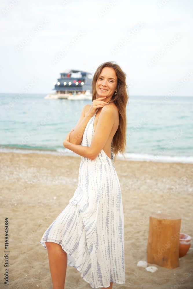 Smiling Woman Posing on Sandy Beach in Summer Dress with Ocean and Boat View Smiling Woman Posing on Sandy Beach in Summer Dress with Ocean and Boat View