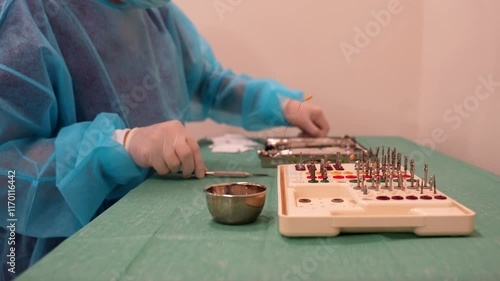 Medium shot of a dentist assistant wearing a PPE suit carefully organizes the tools and material for the doctor for an implant photo